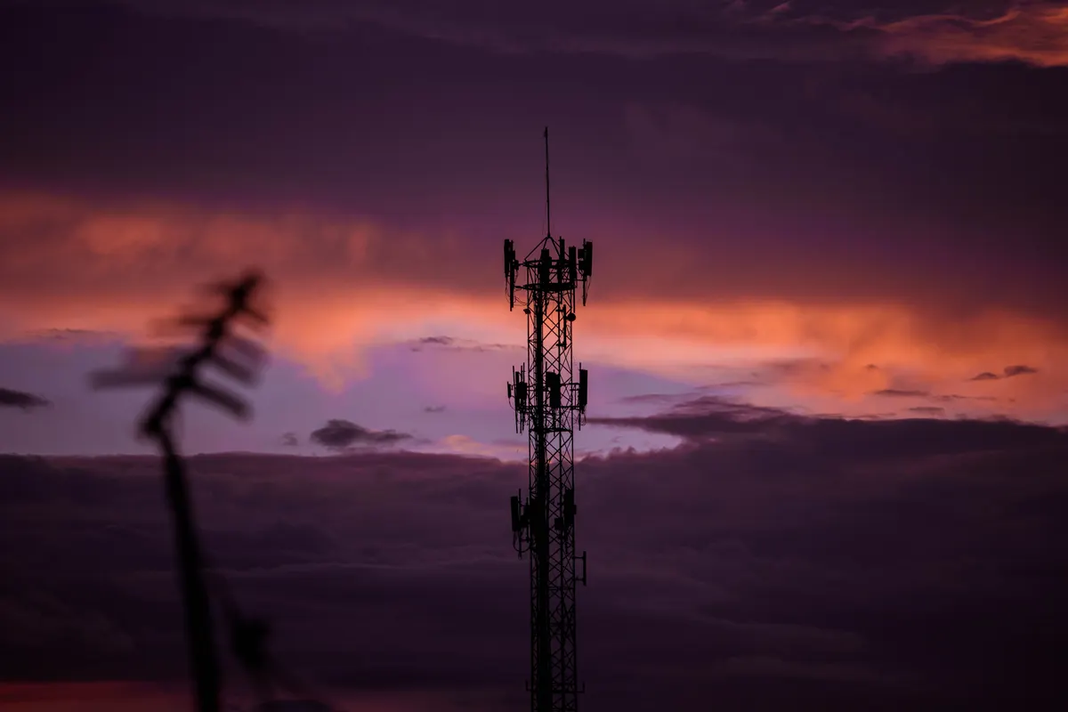 Silhouette eines Mobilfunkmasts mit Antennen vor violett-orangem Abendhimmel