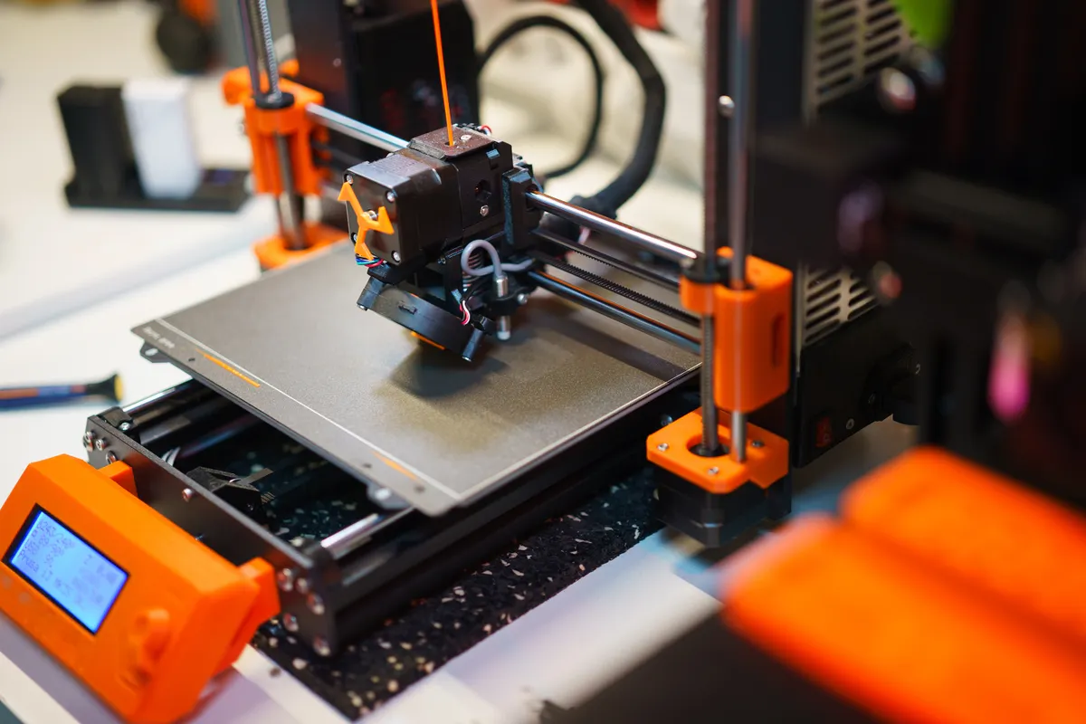 3D-Drucker beim Druck eines orangen Bauteils